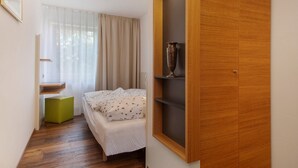 A bedroom with a bed, a green ottoman, a wooden wardrobe, and a window with curtains. - Obst- und Ferienhof Lehle – Apartment Jonagold with Shared Terrace, Garden & Wi-Fi (Immenstaad am Bodensee)