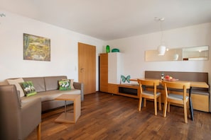 A modern living room with a sofa, a dining table with chairs, a wooden cabinet, and a painting on the wall.
