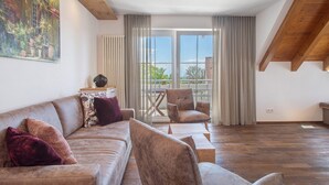 A spacious living area with a high ceiling, a large window with curtains, a wooden ceiling, and a sofa with cushions.