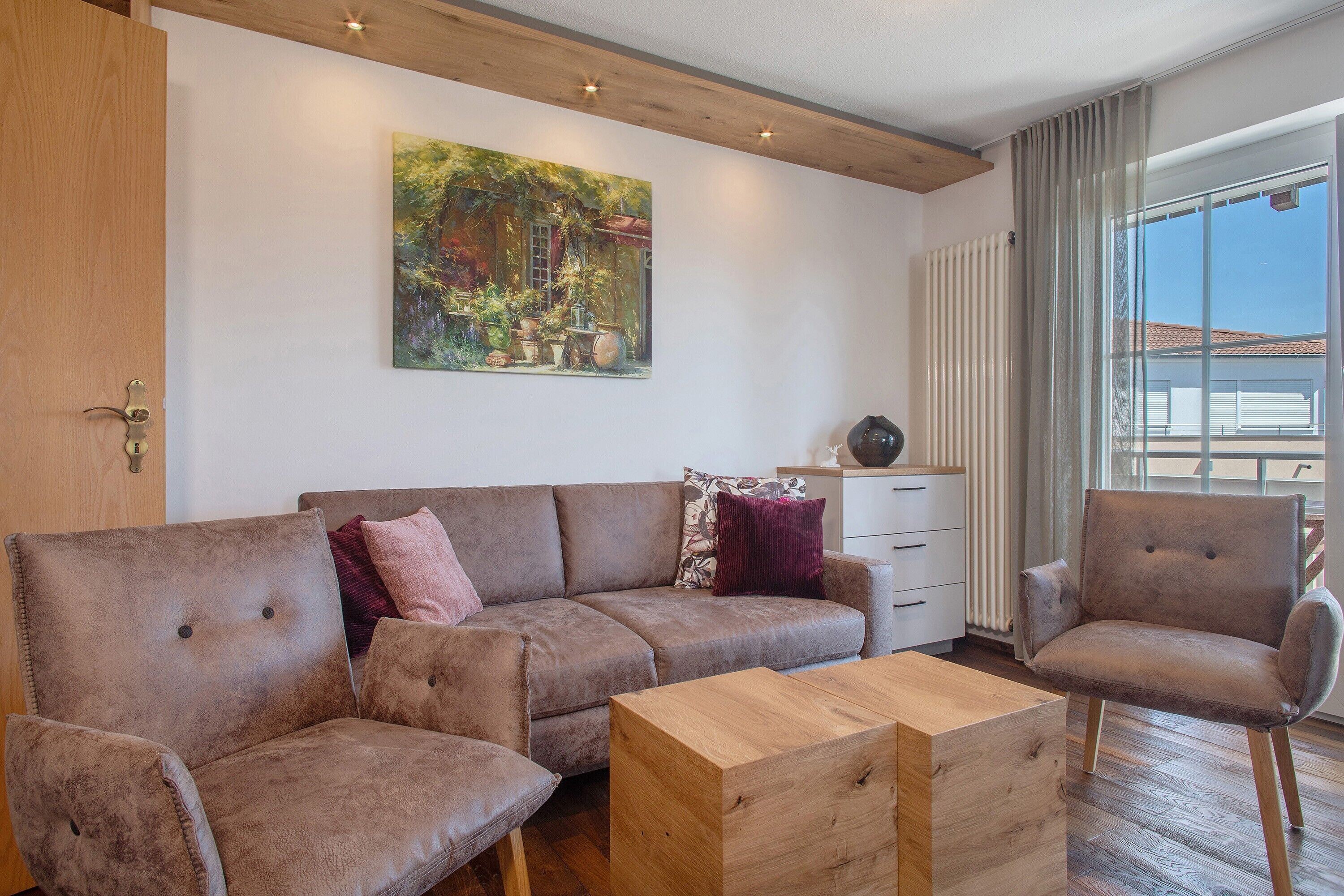 Ein Wohnzimmer mit einer Couch, einem Couchtisch, einem Sessel, einem Gemälde und einem Fenster mit Vorhängen.