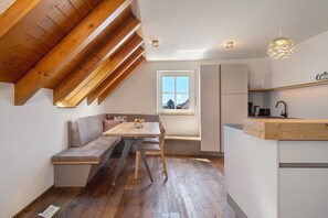 A loft-style room with a wooden ceiling, a dining table, a bench, and a kitchen area with a window. - Apartment 'Wohnung Elstar' with Shared Terrace, Shared Garden and Wi-Fi (Immenstaad am Bodensee)