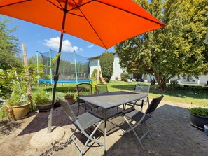 Une terrasse extérieure avec une table et des chaises, entourée de plantes en pot et d’un trampoline.