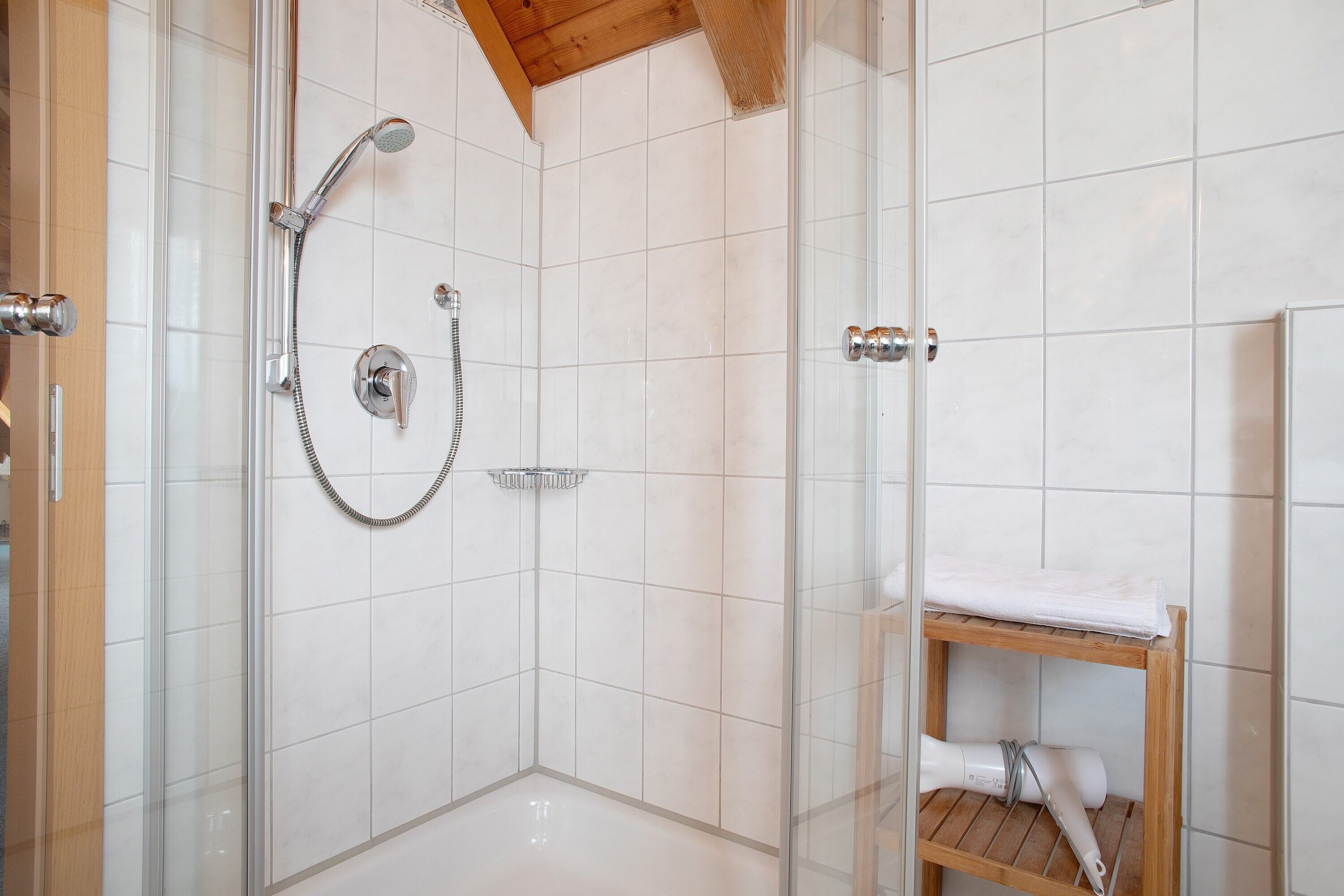 Ducha con mampara de vidrio, cabezal de ducha de mano y grifo empotrado.