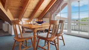 A dining area with a wooden table and chairs, a bowl of fruit, and a view through large windows. - Obst- und Ferienhof Lehle - Apartment Bodensee with Shared Terrace, Garden and Wi-Fi (Immenstaad am Bodensee)