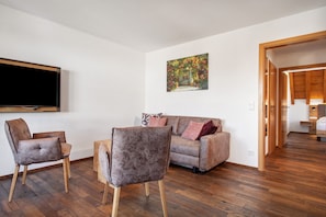 A living room with a sofa, two armchairs, a flat-screen TV, and a painting on the wall.