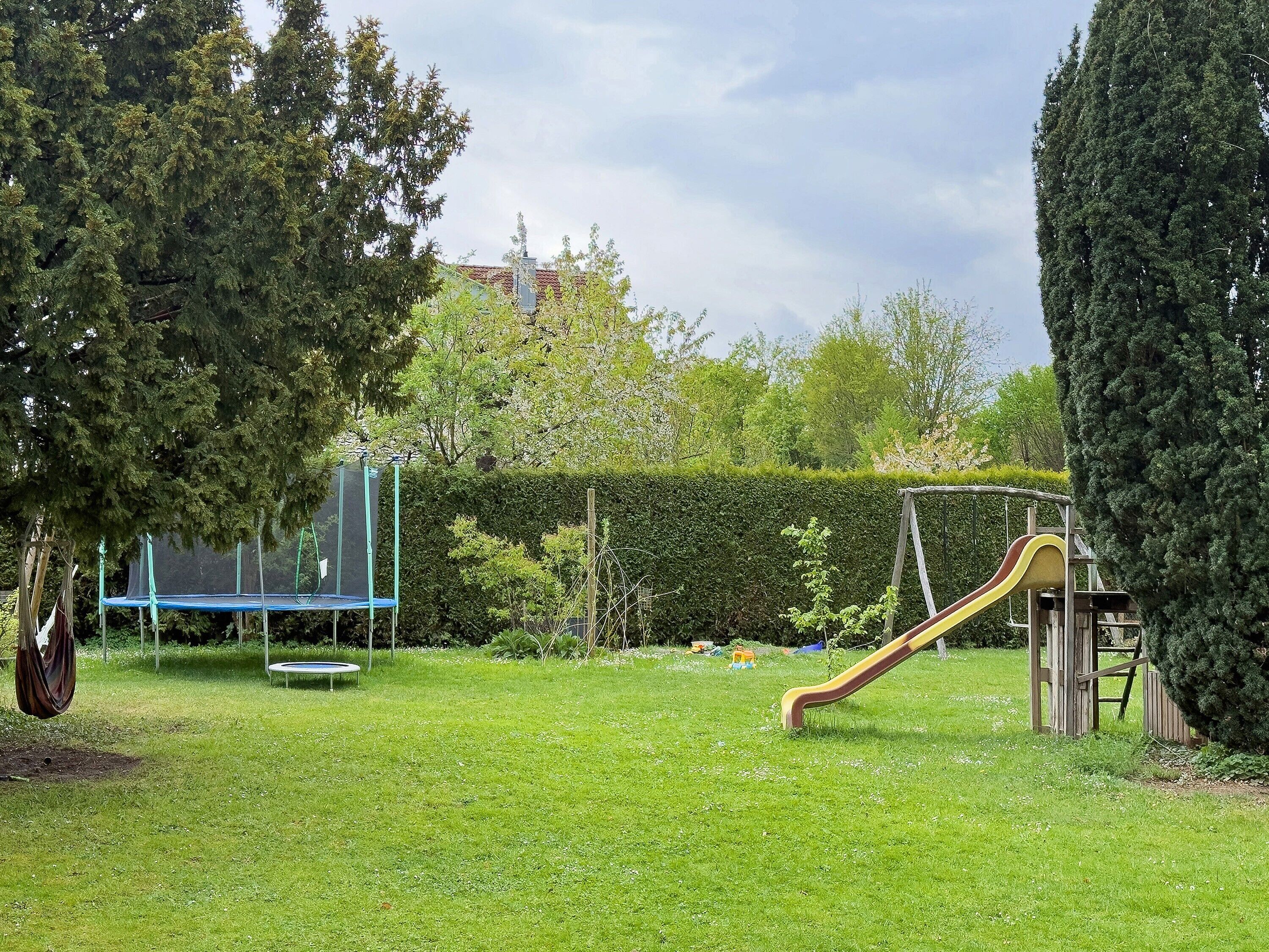 A grassy outdoor area with a trampoline, a slide, and a swing set.