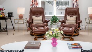 A room with two leather armchairs, a white coffee table, a pink vase with flowers, and a bookshelf with books. - Luxurious Studio in Downtown Douglas (Douglas)