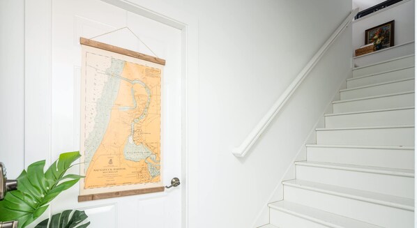 Une porte blanche ornée d’une carte, un escalier et une plante.