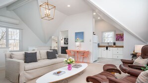 A spacious loft with a high ceiling, a dining area with orange chairs, a kitchen with white cabinets, and a living area with a beige sofa and brown leather chairs. - Luxurious Studio in Downtown Douglas (Douglas)