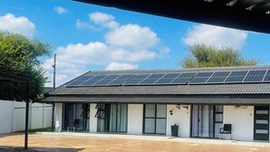A building with solar panels on the roof, a covered patio area, and a small outdoor seating space.