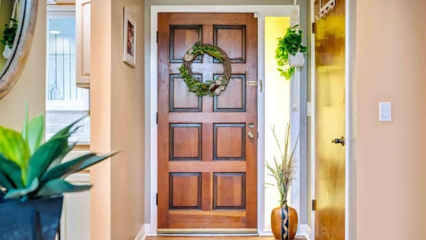 A wooden door with a wreath, a welcome mat, and a potted plant.