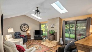 A spacious living room with a ceiling fan, a large clock, a television, and a fireplace.