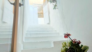 A white staircase leading to a door, a potted plant with red flowers, and a window with a view of a building outside. - San Giovanni Suite Central (Cagliari)