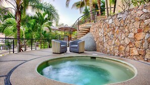 A hot tub area with two striped chairs, a stone wall, and a staircase leading to a balcony.