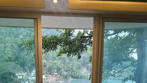 A room with a wooden floor, large sliding glass doors leading to a balcony with a view of a lake and surrounding greenery.