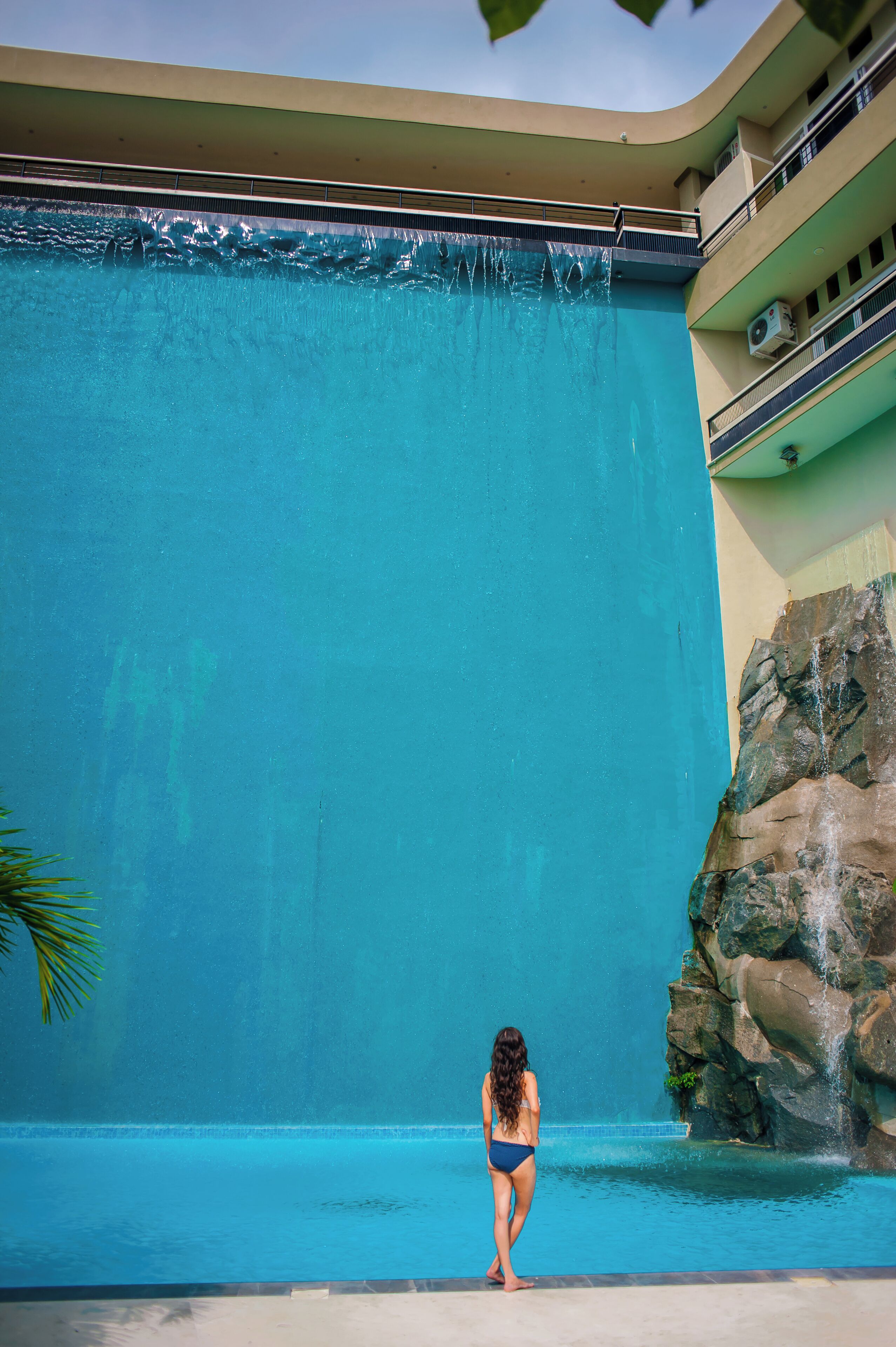 A woman in a swimsuit standing by a pool with a waterfall feature.