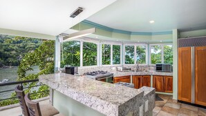 A kitchen with a large island, wooden cabinets, and a view of a river and greenery.