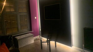 A room with a purple wall, a black sliding door, a window with blinds, a small table, and a bench. - Liverpool City, Fairfield Duplex Suite (Liverpool)