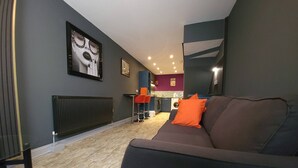 A modern living room with a dark sofa, a red cushion, and a kitchen in the background. - Liverpool City, Fairfield Duplex Suite (Liverpool)