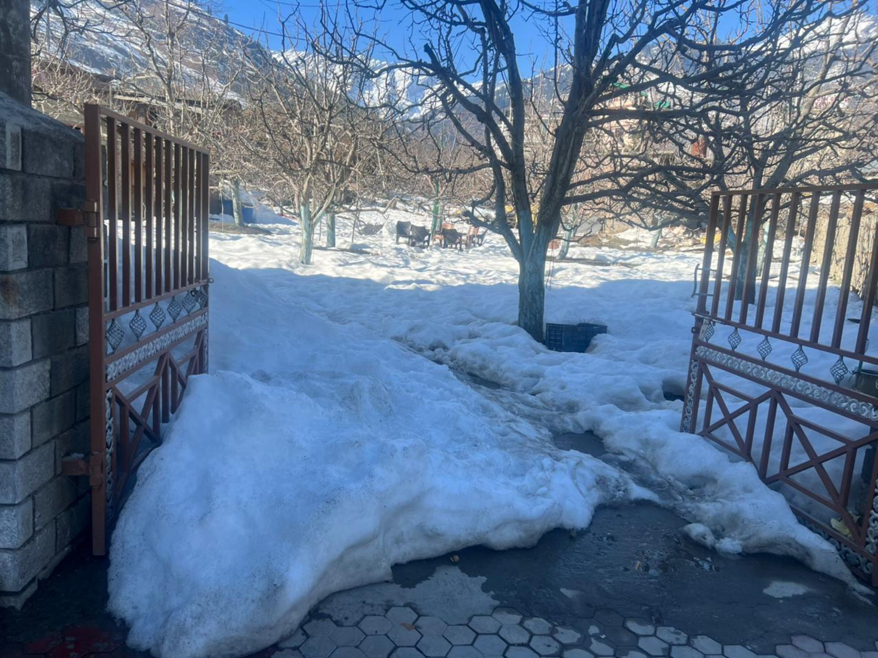 A snow-covered pathway leading to a gated entrance with a brick wall and metal gate.