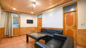Habitació amb sostre de fusta, un sofà de cuir negre, una taula amb superfície de vidre, portes de fusta i un paviment de fusta.