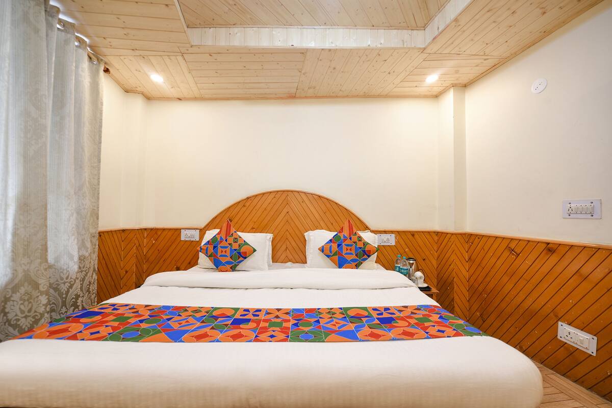 Ein Hotelzimmer mit einem hölzernen Kopfteil, einem Bett mit einer farbenfrohen, geometrischen Tagesdecke und einer schlichten weißen Wand.