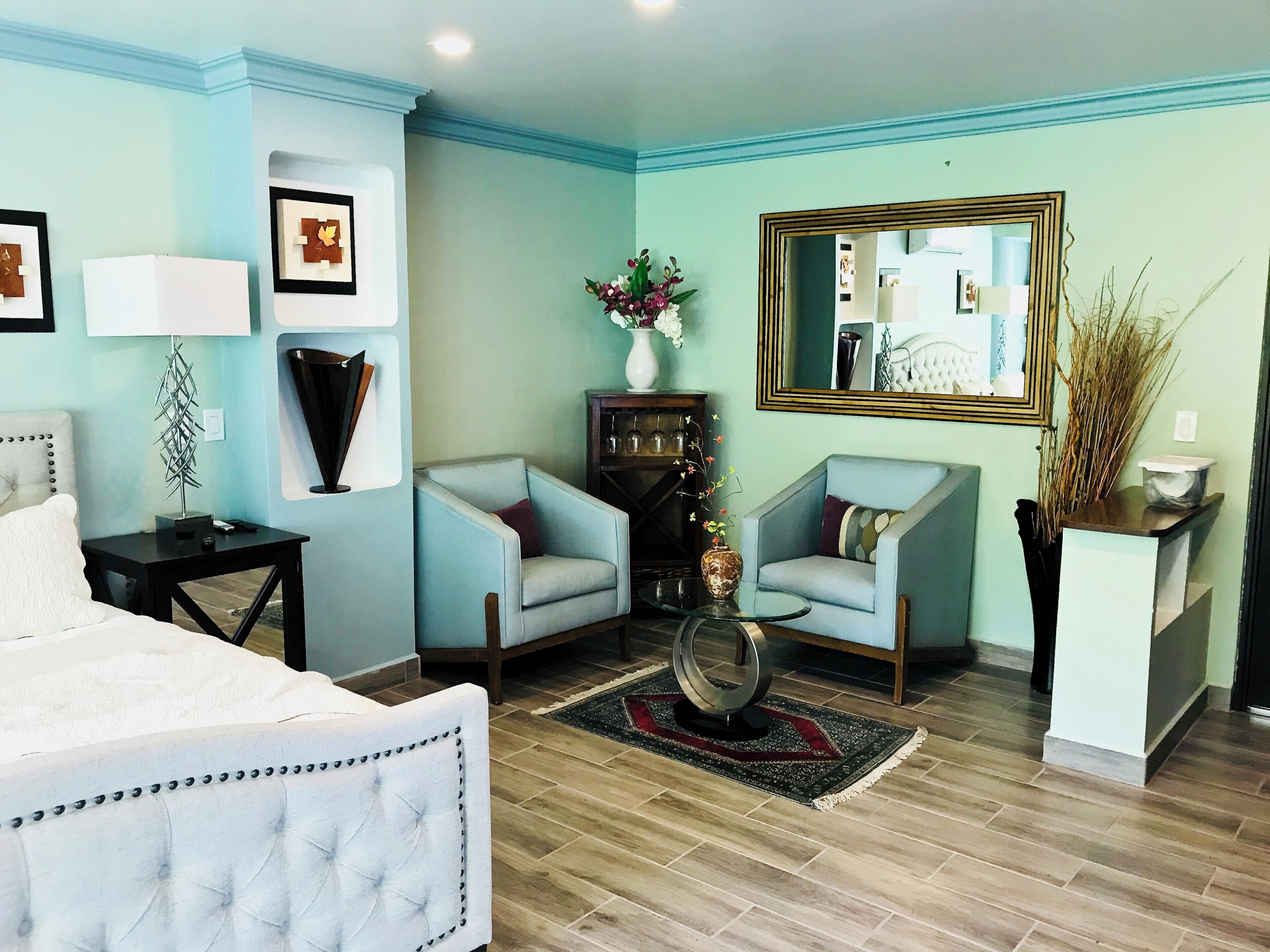 A well-lit living room with a bed, two armchairs, a coffee table, and a mirror.