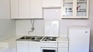 Une cuisine de taille réduite avec des meubles blancs, une cuisinière encastrée et un réfrigérateur.