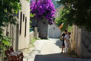 A narrow alleyway with a bench on the left, a woman and a child on the right, and a purple flowering tree in the center. - Apartment Serene Step From The Sea, Sleeps 5 (Tkon)