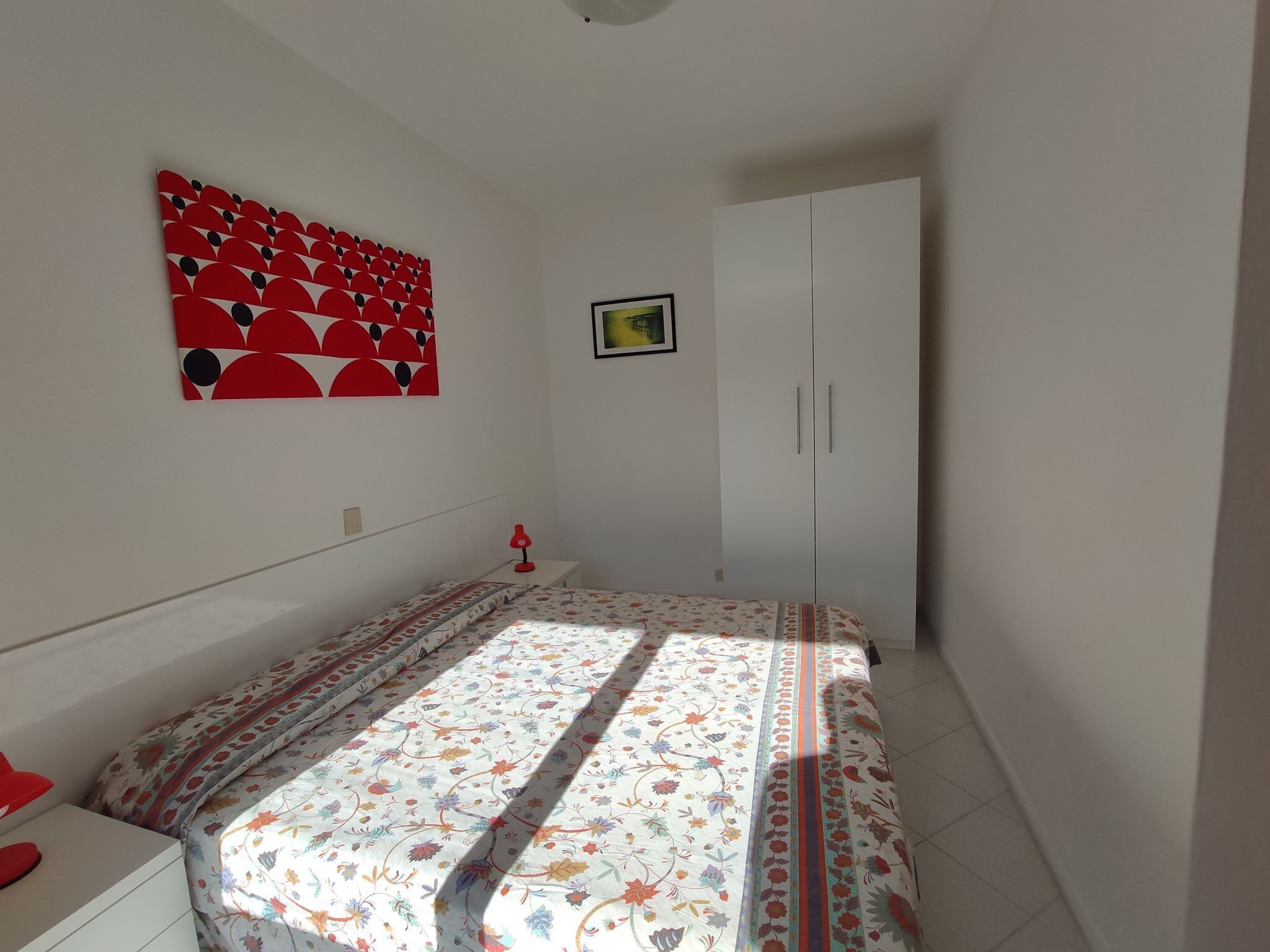 A bedroom with a bed, a wardrobe, a nightstand, and a wall art piece.