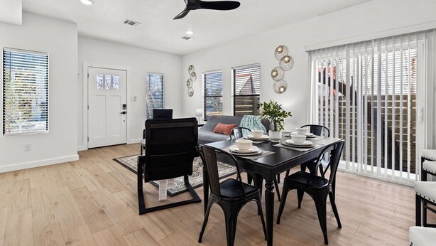 A modern dining area with a black dining table, chairs, and a ceiling fan.
