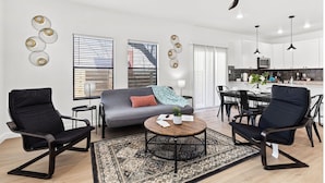 A modern living room with a sofa, two black chairs, a coffee table, and a dining area with a table and chairs.