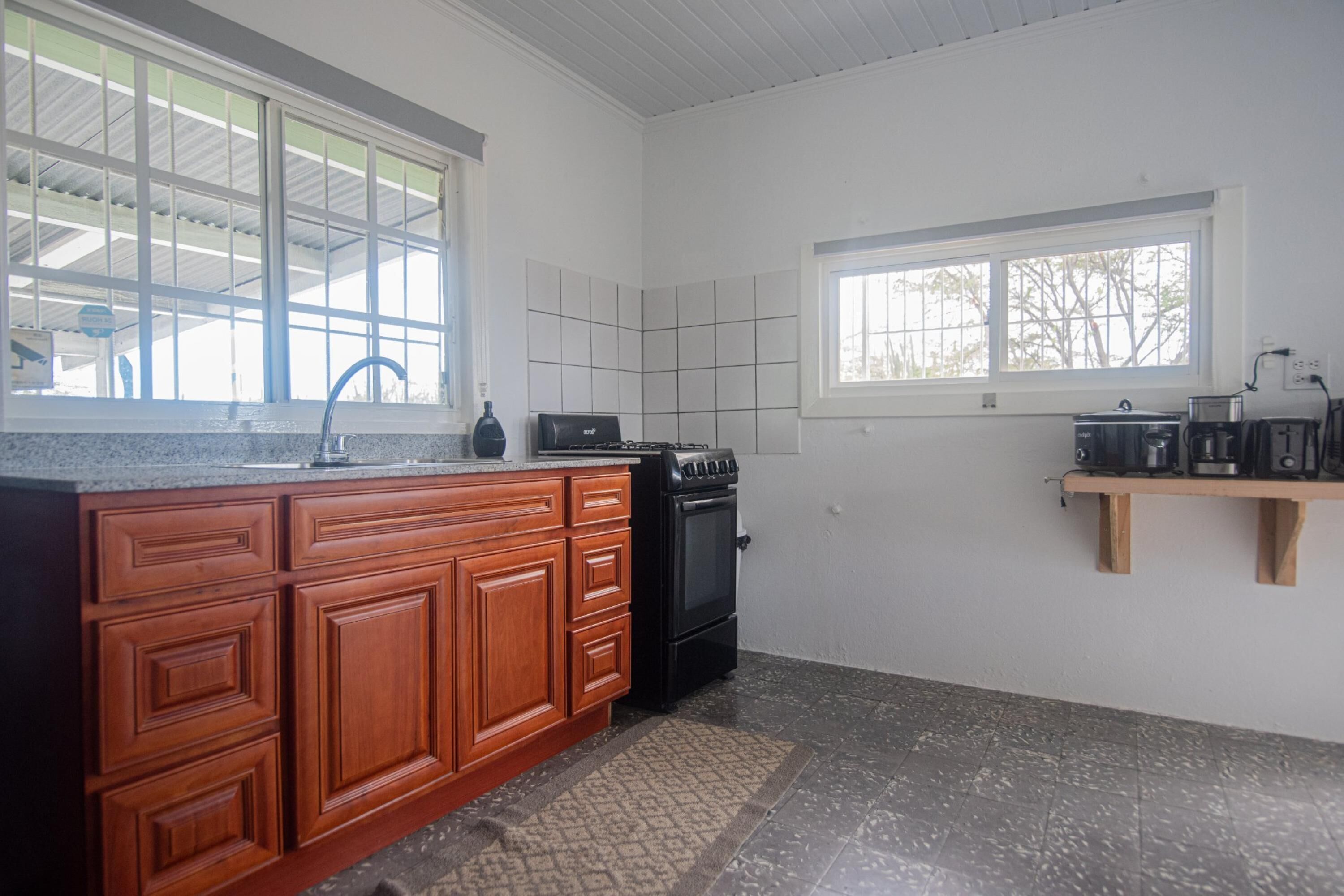 A kitchen with wooden cabinets, a black stove, a tiled backsplash, and a window with a view of trees.