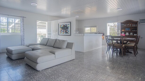 A spacious living area with a large L-shaped sofa, a dining table with chairs, and a kitchen area with a wooden cabinet. - Aruban Home Close to Beach (Oranjestad)