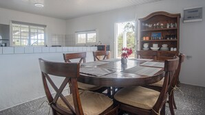 A dining area with a round wooden table, cushioned chairs, and a wooden cabinet with glassware. - Aruban Home Close to Beach (Oranjestad)