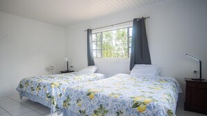 A bedroom with two beds, a window with curtains, a bedside table with a lamp, and a nightstand. - Aruban Home Close to Beach (Oranjestad)