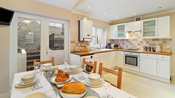 A modern kitchen with white cabinets, a dining table set for a meal, and a view through the glass door.