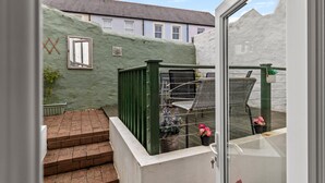 A view from inside a room looking out to a balcony with a green wall, a window, and outdoor seating.