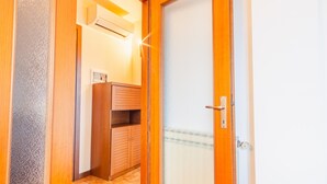 A wooden door with a keyhole and a handle, leading to a room with a wooden cabinet and an air conditioning unit mounted on the wall.