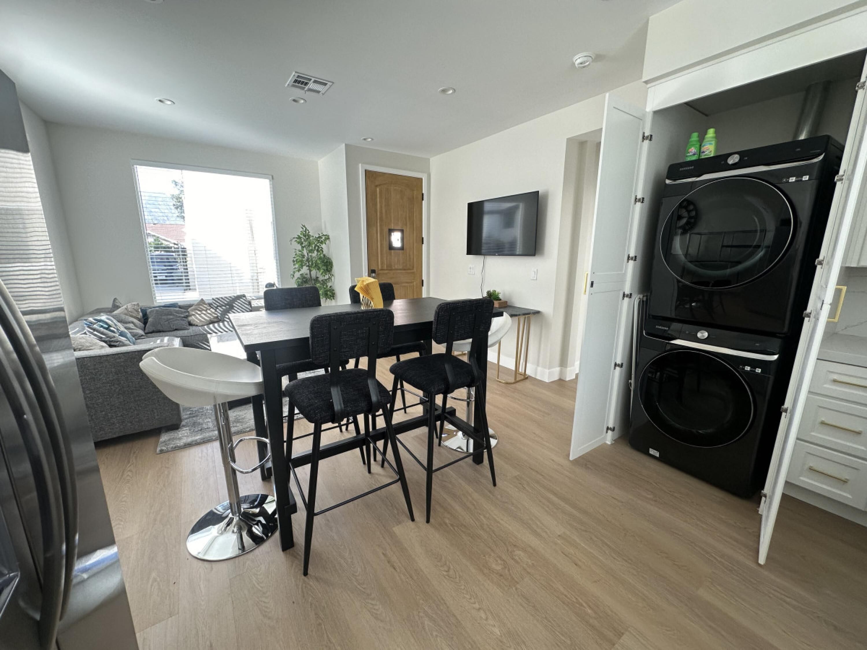 Eine moderne Küche mit integriertem Waschmaschine und Trockner, einem Essbereich mit Tisch und Stühlen sowie einem Wohnbereich mit Sofa und Fernseher.