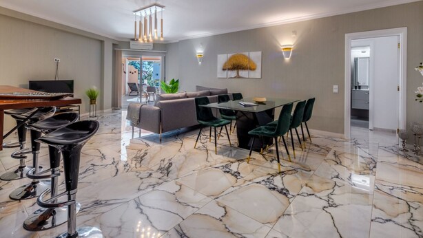 A spacious living area with a marble floor, a sofa, a dining table with chairs, and a television.