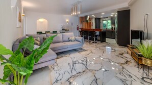 A modern living room with a grey sofa, a marble floor, and a kitchen area with a bar.