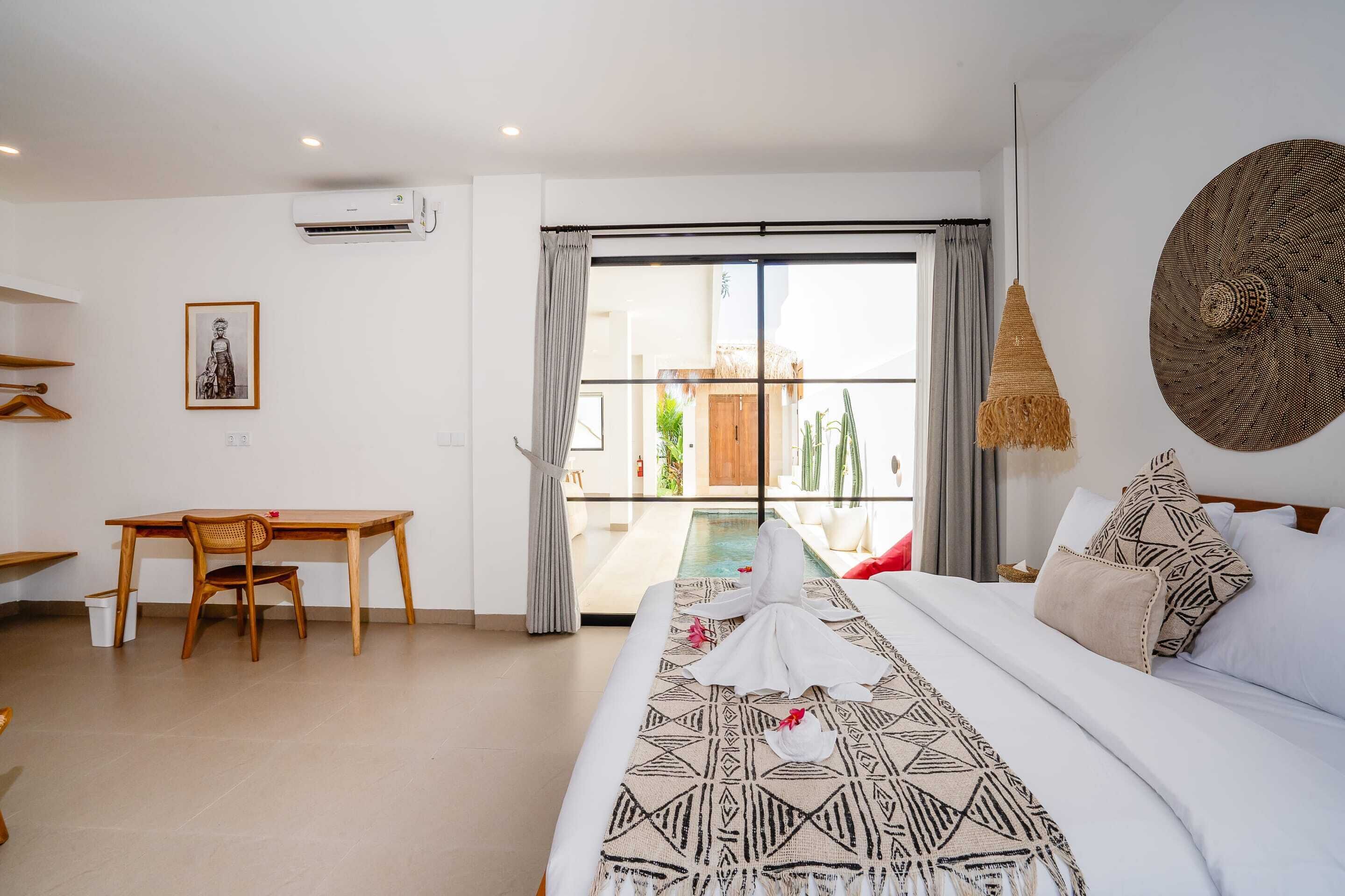 Une chambre avec un lit, un bureau et une chaise. Il y a une fenêtre avec des rideaux, un luminaire suspendu et un climatiseur fixé au mur.