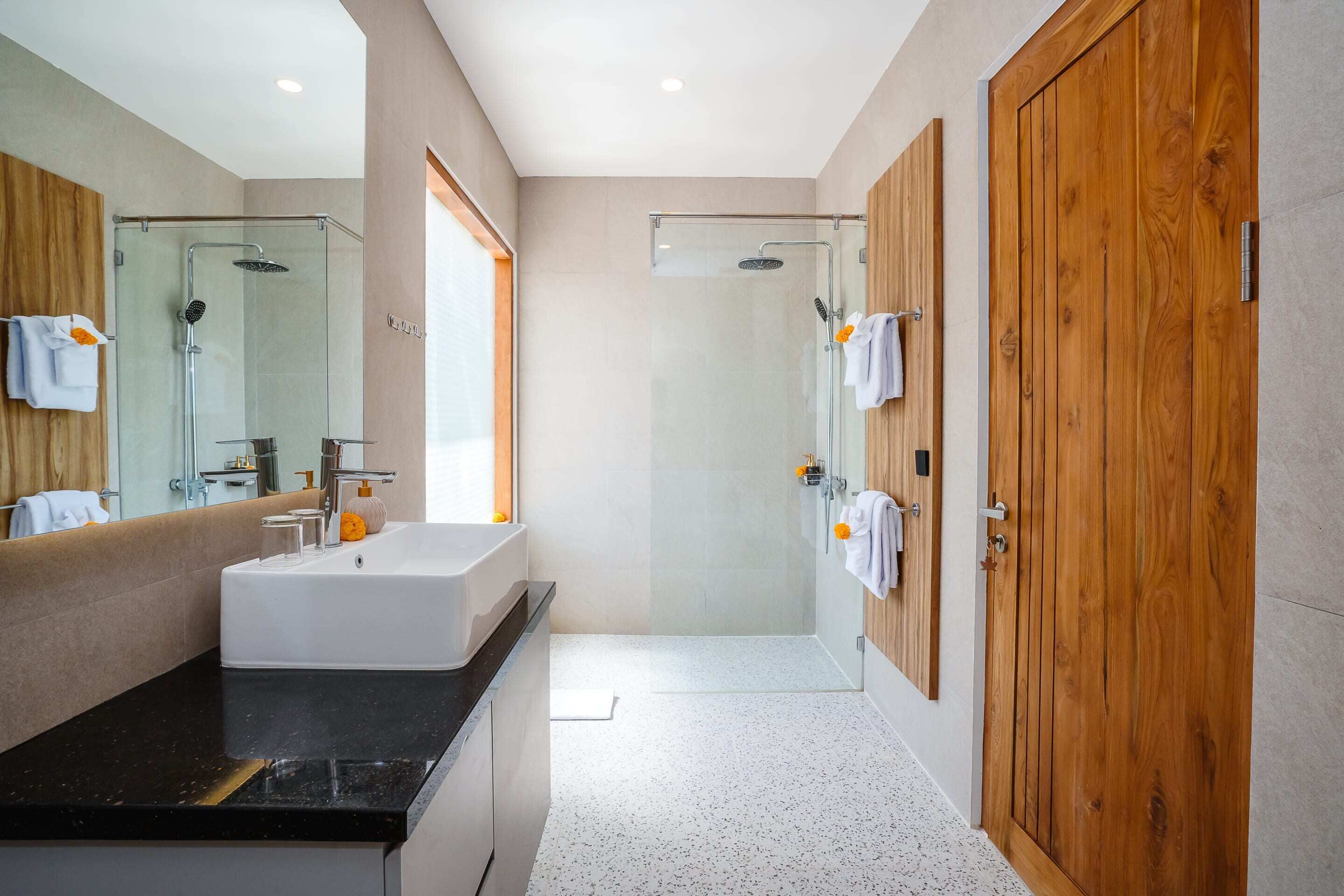 Une salle de bain moderne avec un grand miroir, un lavabo blanc, une douche à parois de verre et des portes en bois.
