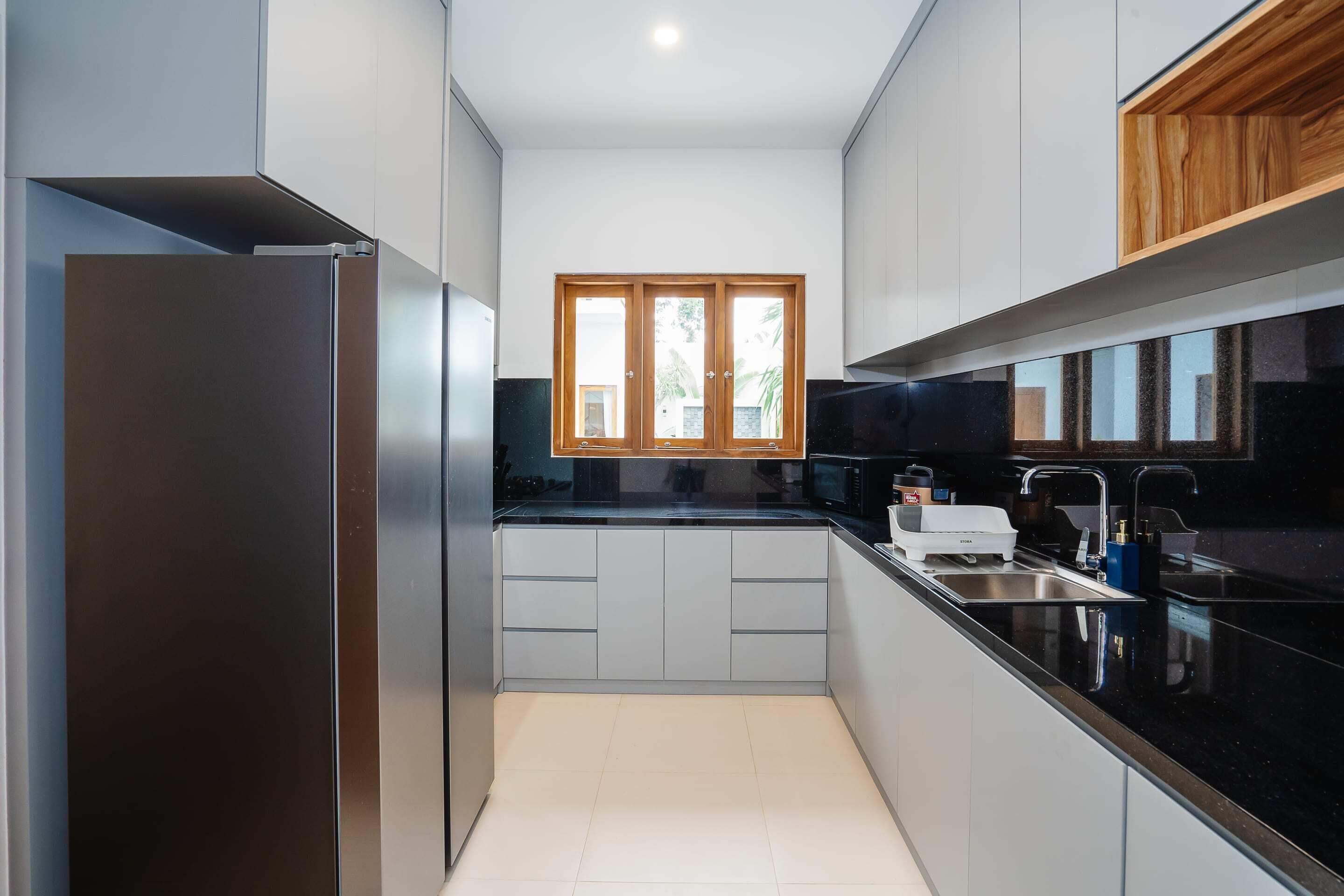 A modern kitchen with a stainless steel refrigerator, a black countertop, and a window with wooden frames.