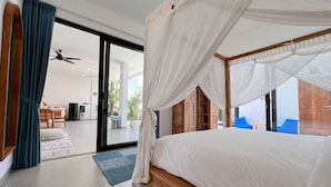 A bedroom with a large bed, a canopy, a sliding glass door leading to a balcony, and a dining area visible through the door. - Villa Timatou (Canggu)