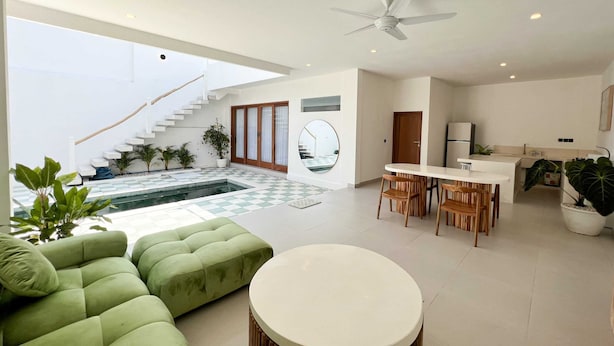 A modern living room with a green sofa, a round table, and a staircase leading to an upper level. - Villa Soleil (Canggu)
