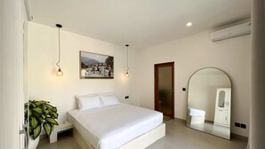 A bedroom with a bed, bedside plant, wall-mounted light, air conditioning unit, and a mirror reflecting a wardrobe. - Villa Soleil (Canggu)