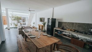 A modern kitchen with a wooden dining table set for four, a built-in oven, and a large TV mounted on the wall. - Villa Mood (Canggu)