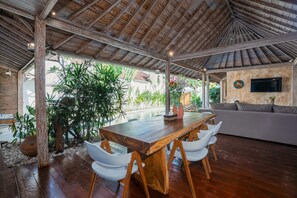 Enjoy meals at the central dining table, surrounded by a view of lush greenery through the large window.